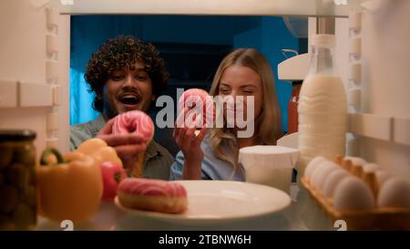 Point de vue POV de l'intérieur réfrigérateur couple multiracial homme indien diverse et femme fille caucasienne à la cuisine de nuit réfrigérateur ouvert manger Banque D'Images