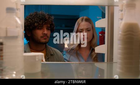 Point de vue POV à l'intérieur du réfrigérateur fille caucasienne femme petite amie femme et homme arabe gars indien petit ami mari multiracial couple la nuit Banque D'Images