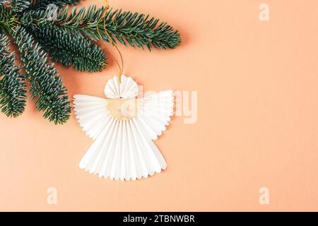 Ange en papier de Noël accroché sur la branche d'arbre sur fond de couleur Peach Fuzz. Concept de vacances de Noël. Vue de dessus. Couleur tendance de 2024 année. Banque D'Images