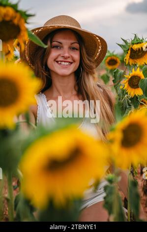 Portrait d'une femme blonde dans un chapeau entouré de tournesols. Banque D'Images
