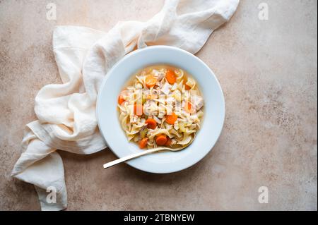 Vue de dessus soupe de nouilles au poulet dans un bol blanc sur fond beige. Banque D'Images