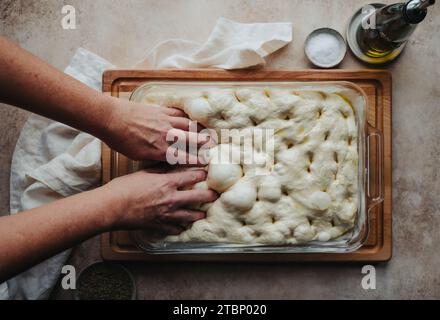 Mains faisant des trous dans la pâte focaccia levée prise d'en haut. Banque D'Images