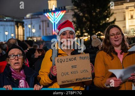 Un manifestant chante des chants de Noël tout en tenant une pancarte pendant la manifestation sur le Trafalgar Square à Londres. Les activistes de extinction Rebellion ont organisé une manifestation lors de la cérémonie officielle des lumières de Noël pour protester contre les plans d'Equinor, basé en Norvège, de développer le champ pétrolifère de Rosebank au Royaume-Uni. Banque D'Images