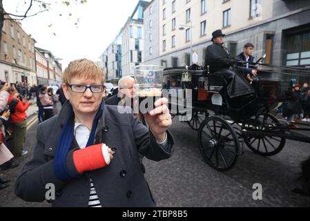 Une femme tient une pinte de Guinness sur Pearse Street alors que la procession funéraire de Shane MacGowan fait son chemin dans les rues de Dublin avant ses funérailles dans Co Tipperary. L'auteur-compositeur, qui a trouvé célèbre en tant que chanteur principal du groupe de punk/folk londonien irlandais The Pogues, est décédé à l'âge de 65 ans la semaine dernière. Date de la photo : Vendredi 8 décembre 2023. Banque D'Images