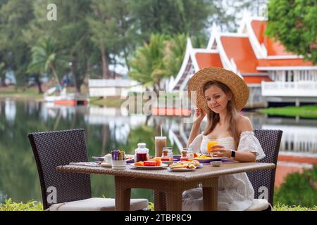 Femme profitant du petit déjeuner à la station tropicale avec vue sur le lac. Banque D'Images