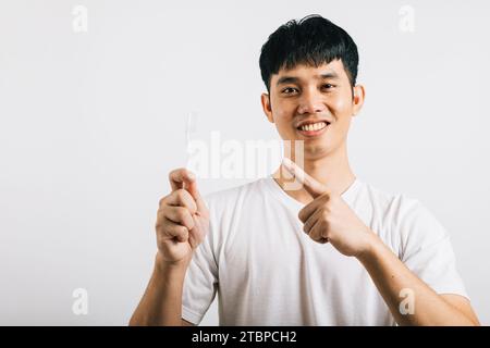 L'homme asiatique se brosse les dents le matin, tient une brosse à dents, sourit et pointe Banque D'Images