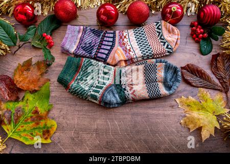 Deux paires de chaussettes d'hiver en laine colorée avec décorations de Noël et feuilles tombées sur un fond de bois. Banque D'Images