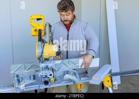 Couper les moulures de base avec la scie à découper est une tâche effectuée par l'ouvrier de coupe Banque D'Images