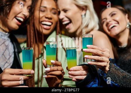 mise au point sélective des verres à shot près des amies multiethniques joyeuses sur fond flou Banque D'Images