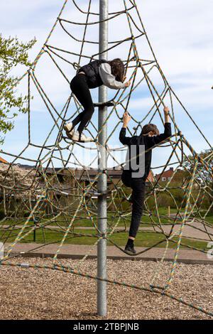 Les deux enfants jouent sur une structure d'escalade extérieure dans un parc urbain public Banque D'Images