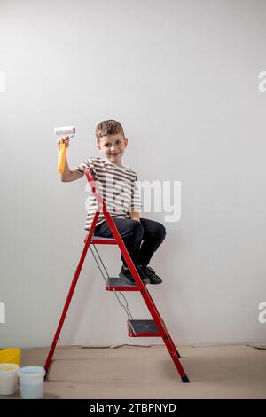 Un constructeur d'enfants se tient sur une échelle et peint les murs blancs d'un appartement. Un enfant avec un rouleau à peinture pendant la rénovation. Banque D'Images