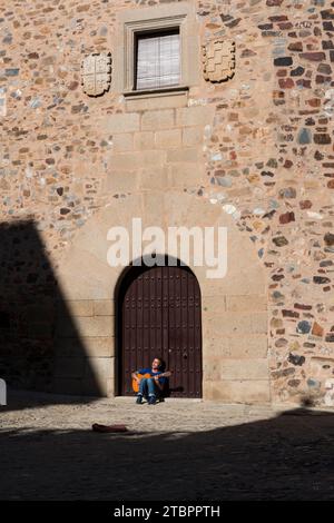 Musicien de rue assis contre la porte de la Casa de los duques de Valencia jouant de la guitare. Caceres, Estrémadure, Espagne. Banque D'Images