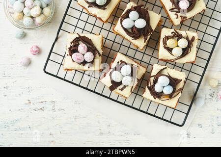 Barres de gâteau aux carottes de Pâques décorées avec nid de chocolat et œufs de bonbons au chocolat fleurissant des fleurs de cerise ou de pomme sur des fonds rustiques en bois clair. Banque D'Images