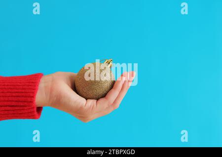 Boule de Noël brillante dorée dans la main d'une femme, décoration de Noël, fond bleu, nouvel an. Décoration de Noël, gros plan pour sapin de Noël. Bannière, Banque D'Images