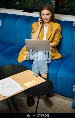 Belle jeune femme utilise un téléphone portable et un ordinateur portable Banque D'Images