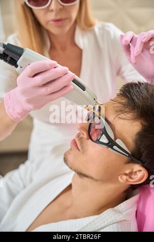 Jeune client du salon de beauté subit la procédure d'épilation faciale laser Banque D'Images