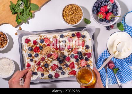 Cuisson faire du yaourt glacé fond d'écorce avec du yaourt grec, des baies fraîches, du granola, du miel, de la sauce au chocolat, avec plaque de cuisson déco. Vue de dessus de la femme Banque D'Images