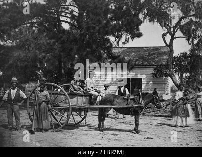 La photo montre un groupe d'esclaves #AfricanAmerican posés autour d'une charrette tirée par des chevaux, avec un bâtiment en arrière-plan, à la plantation de Cassina point de Banque D'Images