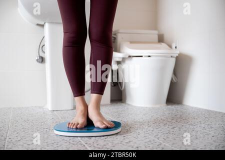 Une femme se tient debout sur une balance dans la salle de bain Banque D'Images