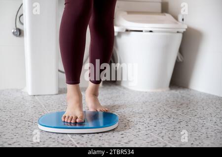 Une femme se tient debout sur une balance dans la salle de bain Banque D'Images