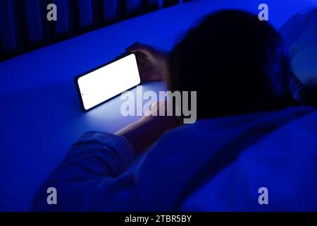 Femme utilisant smartphone couché sur le lit tard dans la nuit dans la chambre avec clair de lune bleu Banque D'Images