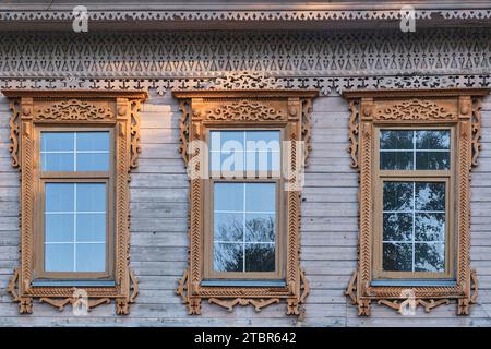 Trois fenêtres typiques avec des plateaux en bois sculpté sur le mur de bord de la maison marchande résidentielle du 19e siècle dans le centre historique de la ville Yelabuga, Ru Banque D'Images