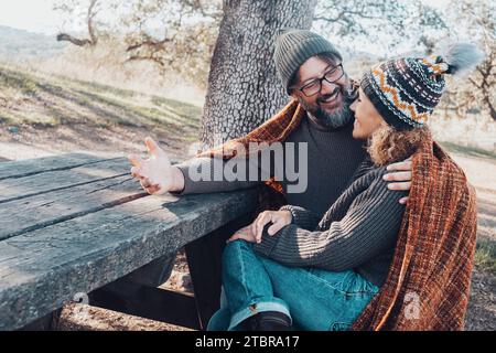 Heureux couple adulte profiter du temps ensemble dans l'activité de loisirs en plein air assis sur un banc en bois et une table au parc en vacances week-end. Homme parlant et racontant à une femme. les gens mariés Banque D'Images