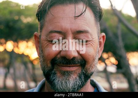 Gros plan portrait d'homme mûr avec barbe et yeux fermés souriant sur la caméra. Bien-être et santé mentale concept bonheur style de vie. Équilibre de vie intérieur positif. Les hommes adultes dans la joie en plein air Banque D'Images