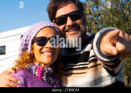 Heureux couple de touristes homme et femme pointant et admirant la destination avec sourire et camping-car van rv camping-car en arrière-plan. Vacances avec véhicule de location. Les gens de vacances d'été Banque D'Images