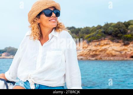 Une jeune adulte jeune femme sereine assise sur un bateau profitant d'une excursion sur le littoral pendant les vacances d'été. Île en arrière-plan. Concept de voyage et de liberté mode de vie les gens à la mer Banque D'Images