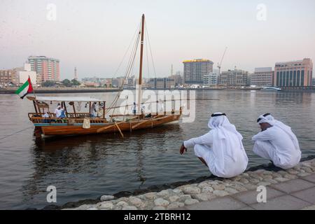 Deux hommes locaux accroupissent sur le rivage du ruisseau dans le quartier historique d'Al Shindagha, Dubaï, Émirats arabes Unis. Banque D'Images
