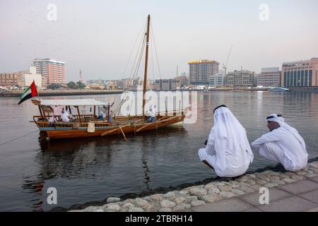 Deux hommes locaux accroupissent sur le rivage du ruisseau dans le quartier historique d'Al Shindagha, Dubaï, Émirats arabes Unis. Banque D'Images