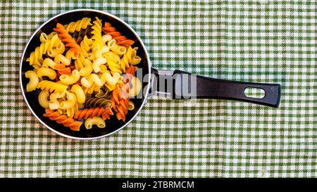 Petite petite poêle à frire avec pâtes fusilli crues tricolores dans une composition rustique. Banque D'Images