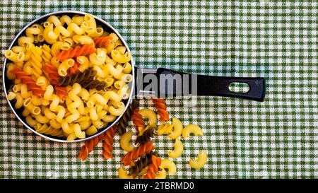 Petite petite poêle à frire avec pâtes fusilli crues tricolores dans une composition rustique. Banque D'Images