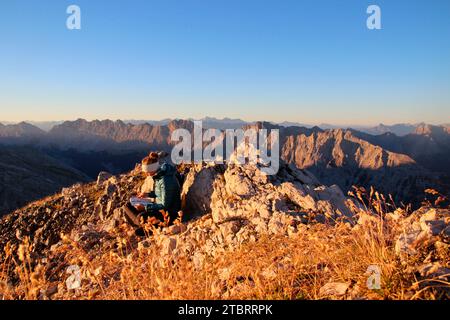 Jeune femme écrivant une entrée dans le livre du sommet, au lever du soleil, vue dans le Karwendel, randonnée à la Pleisenspitze (2569m) vue du sommet chaîne Karwendel fr Banque D'Images