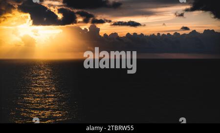 Une scène de coucher de soleil paisible, avec un ciel orange vibrant illuminé par le soleil couchant, projetant sa lueur chaude sur une vaste étendue d'eau bleue nuageuse Banque D'Images