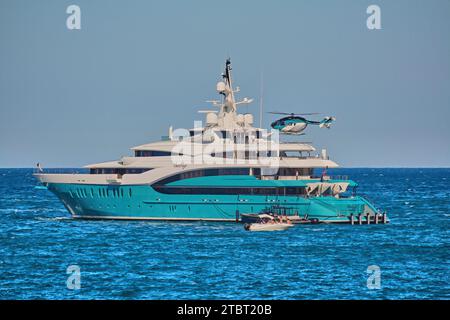 Rayons de soleil de superyacht de 85m à l'ancre avec l'hélicoptère entrant pour atterrir sur l'hélideck. Banque D'Images