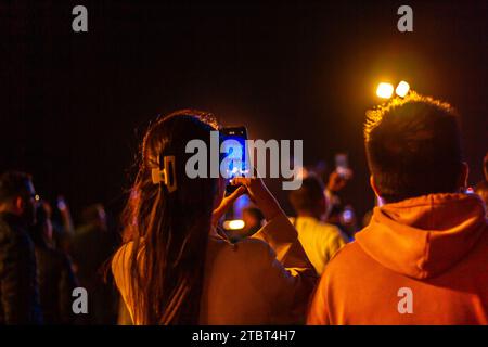 Une jeune femme anonyme enregistrant un spectacle de lumière sur son téléphone la nuit, vue de derrière, en direct depuis son smartphone Banque D'Images