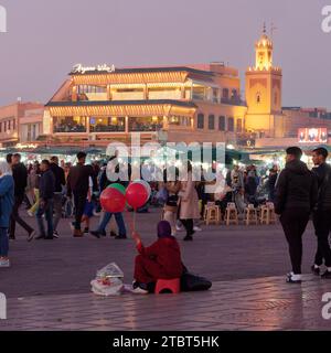 Lady vend des ballons sur la place du marché Jemaa el-Fnaa la nuit avec un restaurant doré derrière à Marrakech aka Marrakech, Maroc, 08 décembre 2023 Banque D'Images