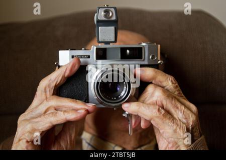 Personnes âgées Old Mans mains tenant la caméra de film Vintage dans l'éclairage intérieur doux Banque D'Images
