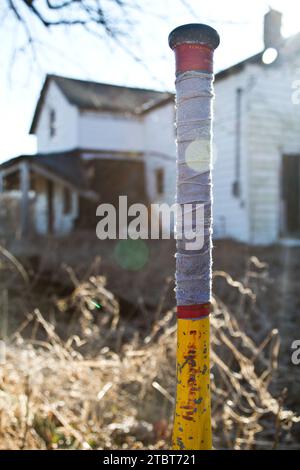 Gros plan d'une batte de baseball patinée contre une maison rurale abandonnée à Golden Hour Banque D'Images