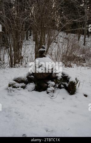 Au milieu des murmures neigeux, des rochers mystiquement empilés ornés de neige et de mousse créent une scène enchanteresse à Pokainu Mezs, Dobele, Latvija Banque D'Images