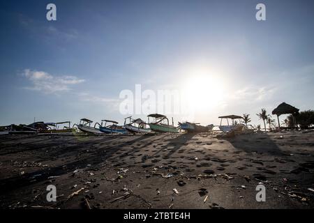 Bateau de pêche traditionnel Jukung, sur une plage de sable noir directement au bord de la mer, paysage du soir au bord de la mer sur l'île tropicale de Sanur, Bali, Indonésie Banque D'Images