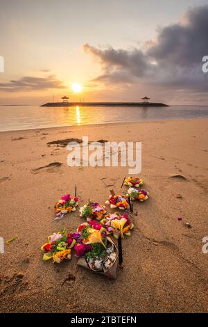Lever de soleil sur une plage de sable avec de petits temples dans l'eau, paysage tourné avec des offrandes de prières hindoues traditionnelles sur la plage de Sanur, Bali, Indonésie Banque D'Images
