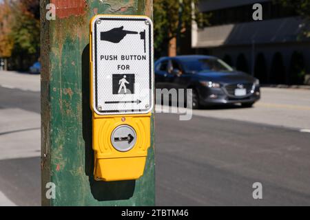 Piéton bouton d'appel poussoir, avec voiture floue en arrière-plan Banque D'Images