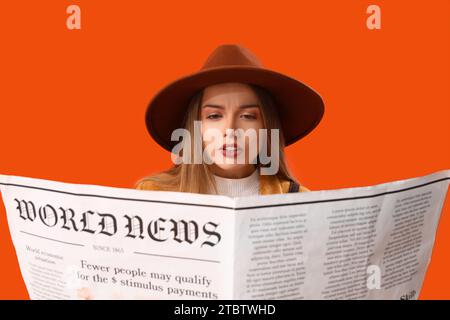 Jeune femme lisant le journal sur fond orange, closeup Banque D'Images