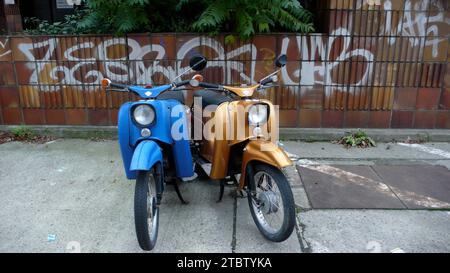 Deux scooters motorisés garés dans le lot devant un mur de briques marqué avec des graffitis. Banque D'Images