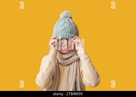 Mignon petit garçon heureux dans les vêtements d'hiver sur fond jaune Banque D'Images