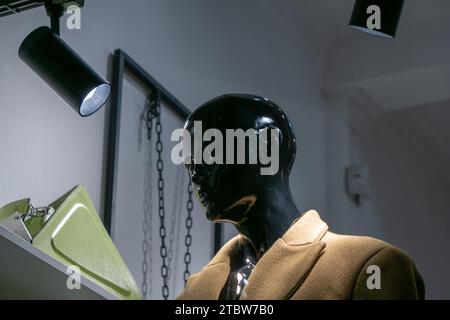 Mannequin femme en plastique noir vêtu d'un manteau de couleur kaki, debout à l'intérieur du magasin de mode. Banque D'Images