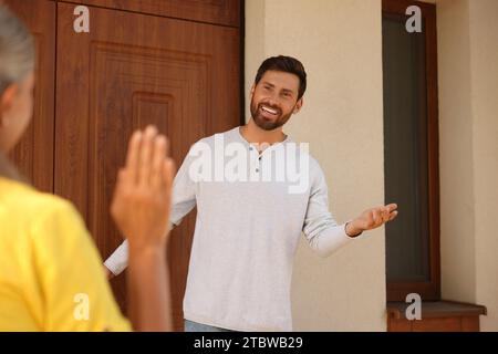 Relation amicale avec les voisins. Homme heureux accueillant femme senior dehors Banque D'Images